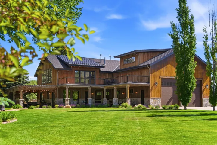 Expansive lawn framing a multi-story residence with a dark metal roof, wood siding, and stone accents