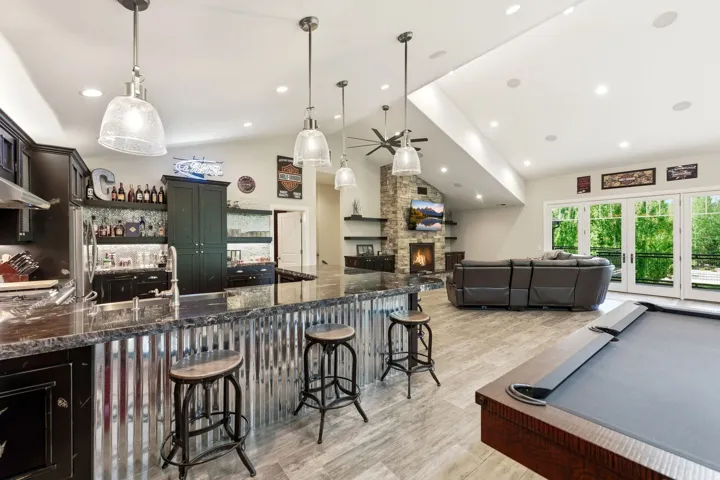 Open-concept space featuring a full wet bar with stone-finish countertops, a stone-clad fireplace, and wood-finish flooring