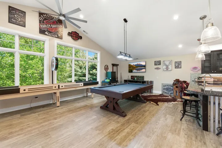 Spacious recreational area featuring vaulted ceilings, large windows, wood-finish flooring, a built-in wet bar with pendant lighting, and recessed lighting