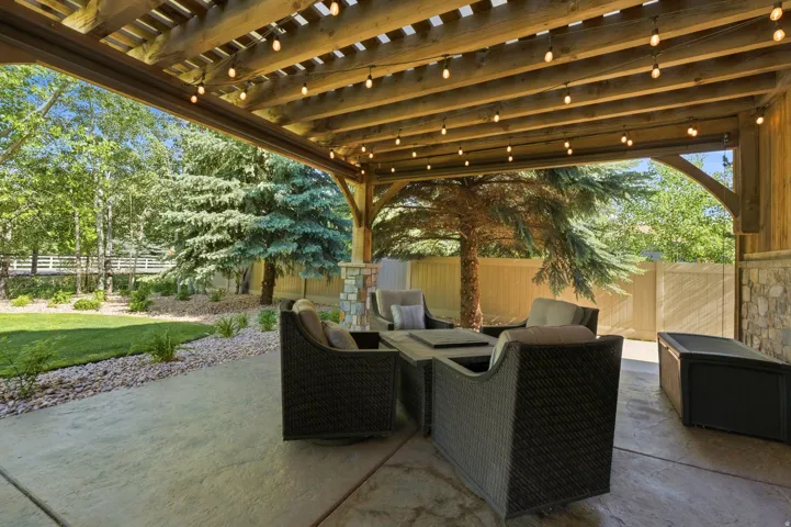 Expansive patio featuring a wood beam pergola with string lighting, concrete flooring, and a stone accent wall