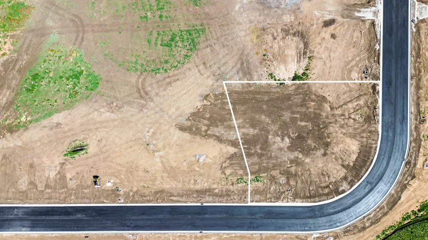 Cleared building lot with delineated property lines, featuring direct frontage on a newly paved street