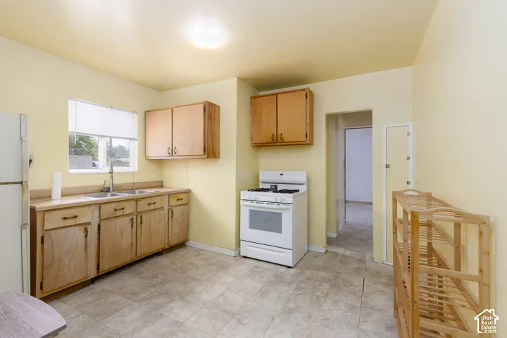Kitchen featuring wood cabinetry, laminate countertops, a double-basin stainless steel sink with a gooseneck faucet, a freestanding white range, and tiled flooring
