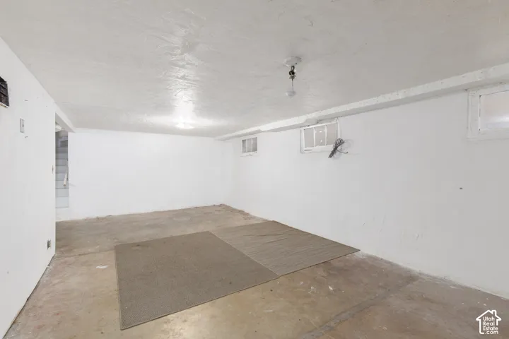 Spacious lower-level room featuring painted concrete flooring, white painted walls, and overhead lighting