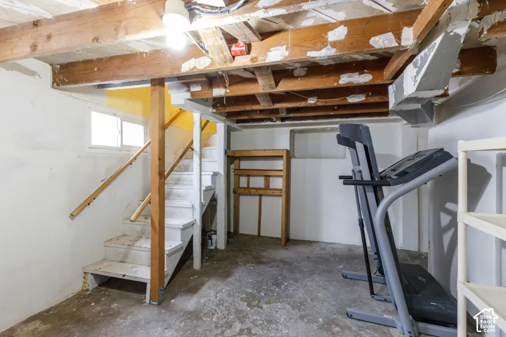 Unfinished basement featuring exposed wood ceiling joists, concrete flooring, and a painted wooden staircase with railing