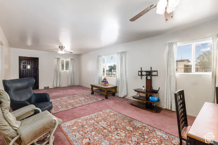Spacious living area featuring wall-to-wall carpeting, multiple windows for natural light, and two ceiling fans