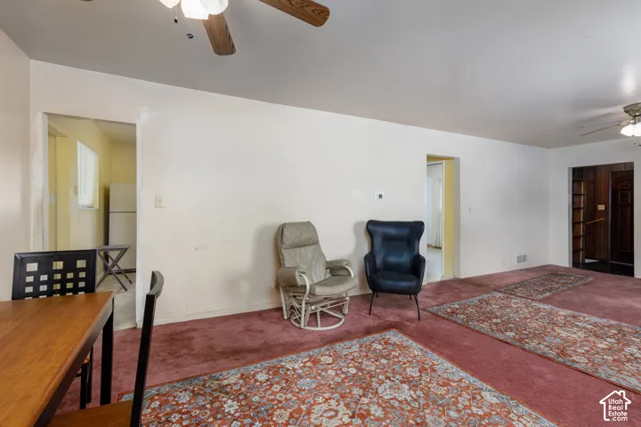 Expansive living area featuring red carpeting, white walls, and a ceiling fan with integrated lighting
