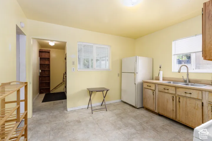 Kitchen area with light-toned tiled flooring, light yellow painted walls, and two windows with horizontal blinds