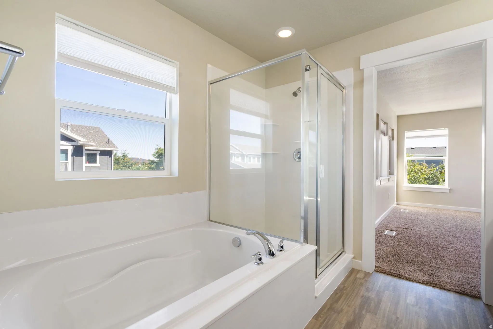 Bathroom featuring a built-in soaking tub with polished chrome fixtures, a glass-enclosed shower, wood-finish flooring, and a window with blinds