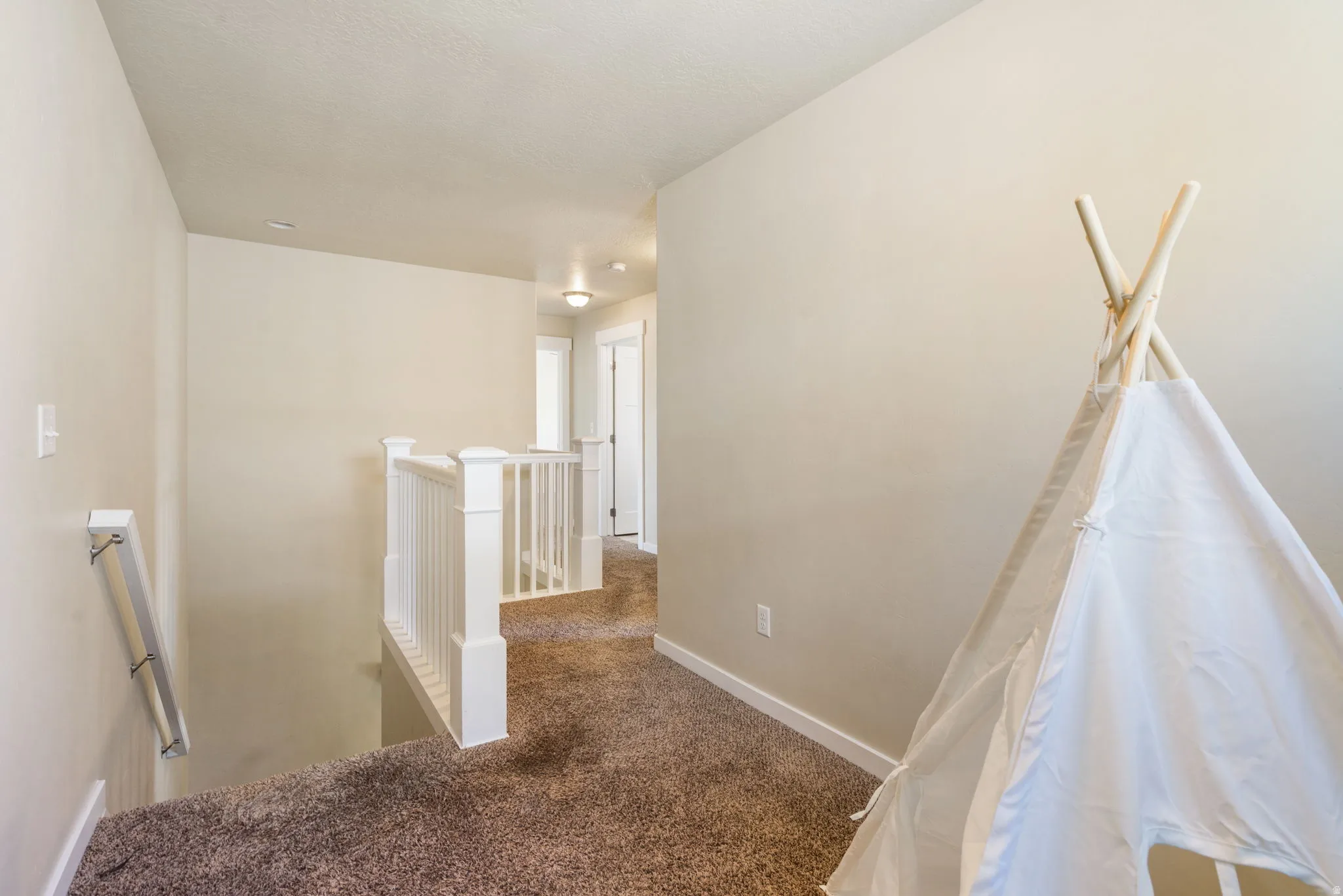 Upper-level hallway featuring plush carpet flooring, white painted balusters and newel posts, and neutral-toned wall paint