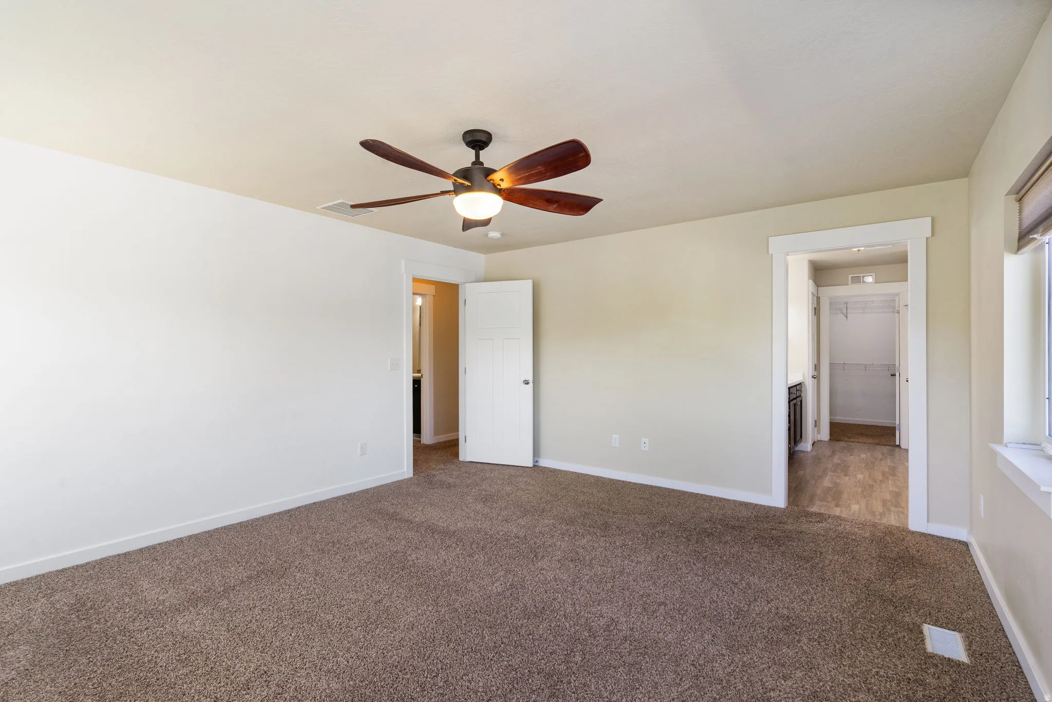 Carpeted room featuring a ceiling fan with integrated lighting, a white paneled door, and a window with blinds