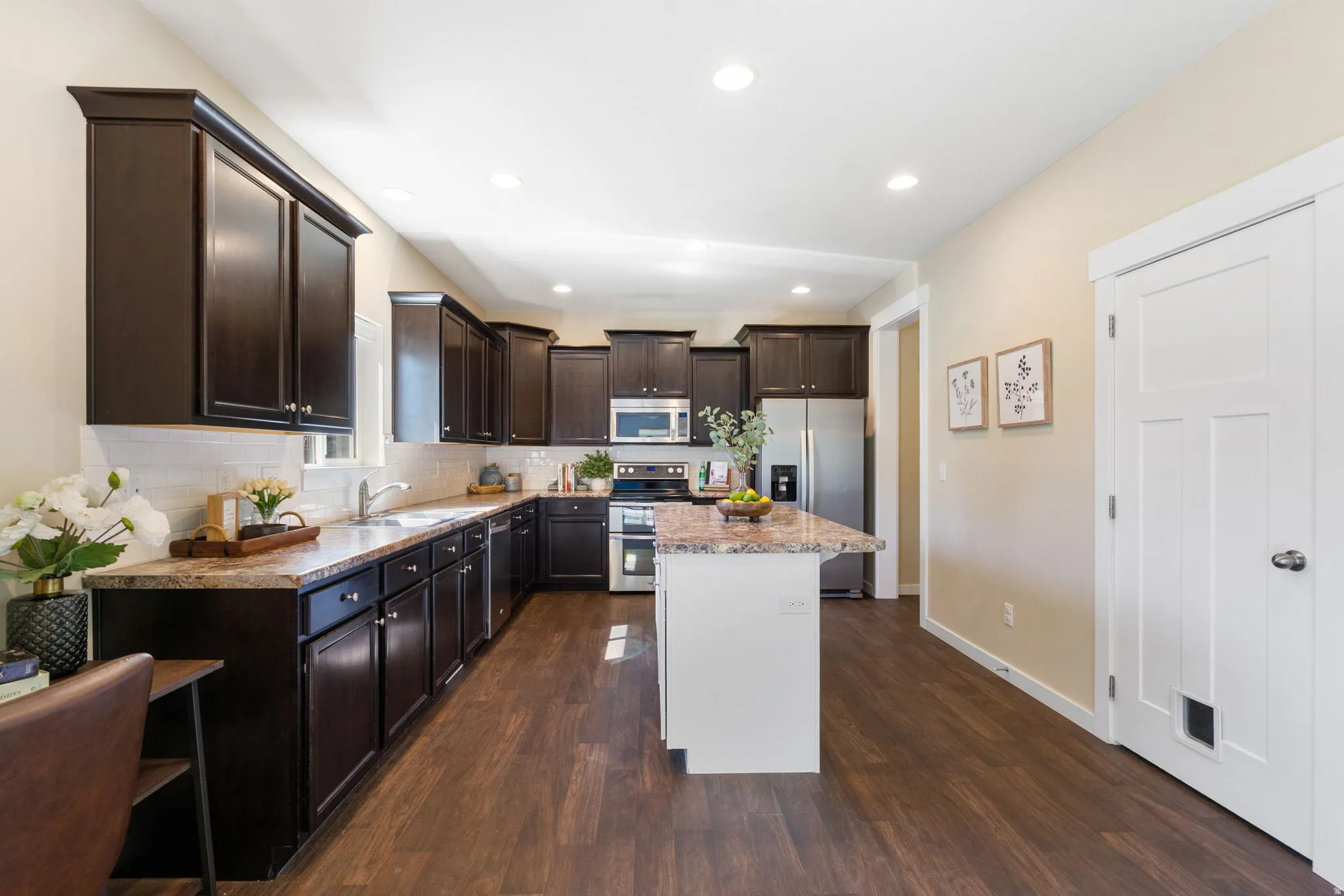 Contemporary kitchen featuring dark wood cabinetry, light countertops, wood-finish flooring, recessed lighting, and a center island with a stone-finish countertop