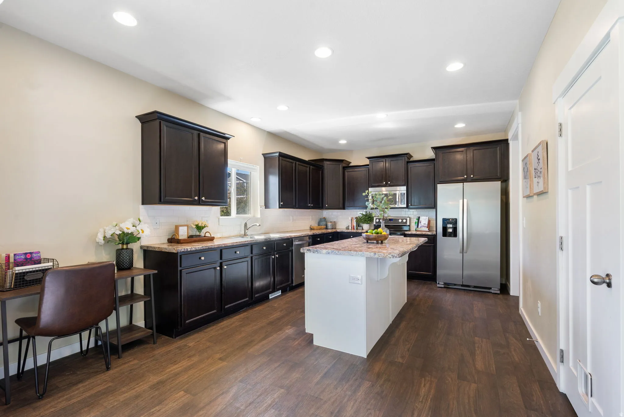 Kitchen featuring wood-finish flooring, dark cabinetry, light-toned countertops, a white subway tile backsplash, and recessed lighting