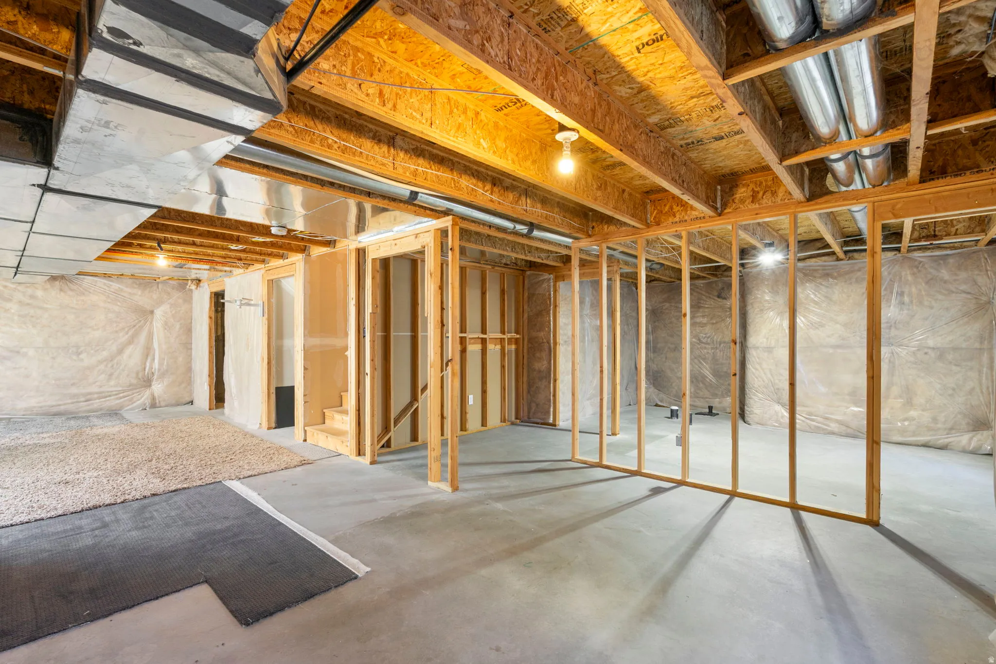 Unfinished basement featuring exposed wood joists, concrete flooring, and partial framing for future development
