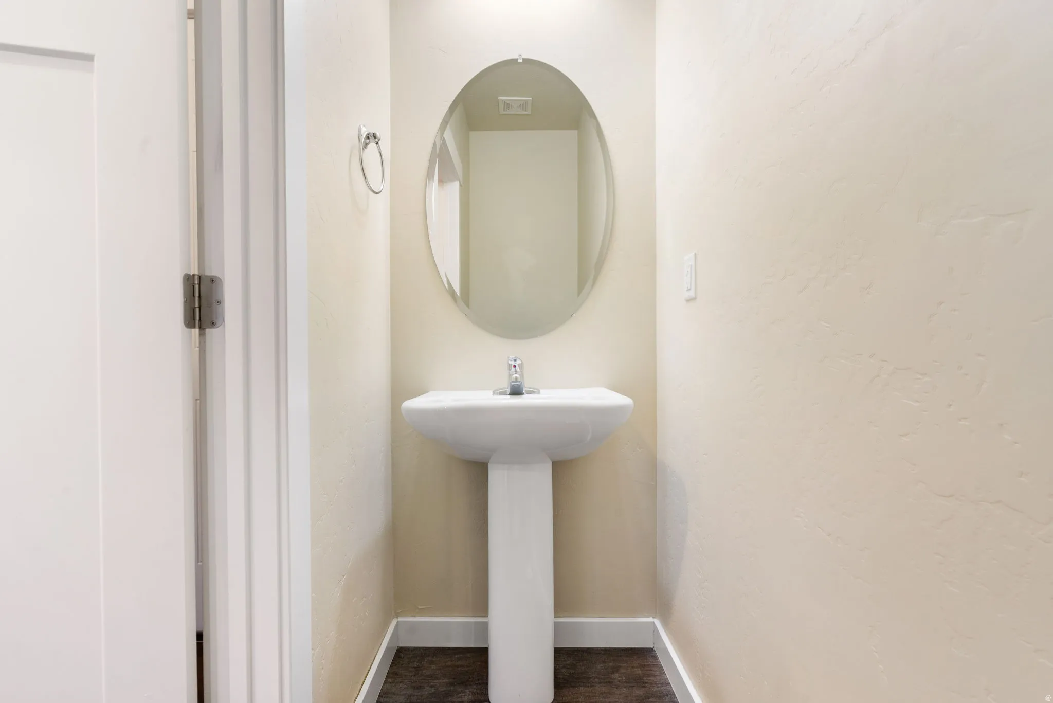 Pedestal sink with a polished chrome faucet, an oval wall-mounted mirror, a towel ring, and wood-finish flooring