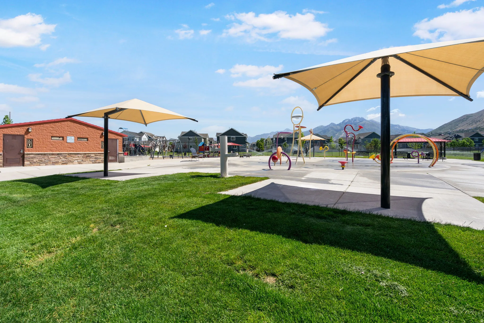 Expansive green space featuring a large shade structure, concrete pathways, and an adjacent brick-and-stone building
