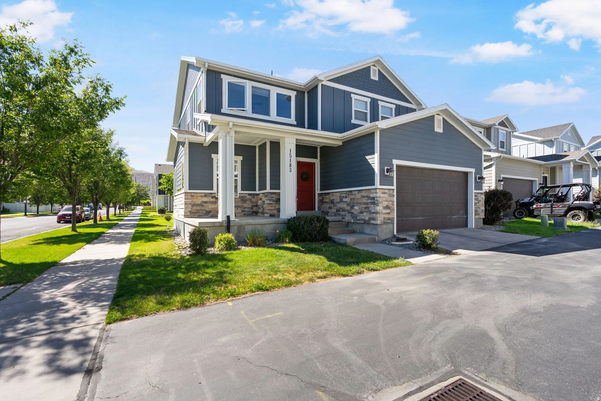 Contemporary two-story exterior featuring blue siding, stone accents, a covered porch, and a two-car garage