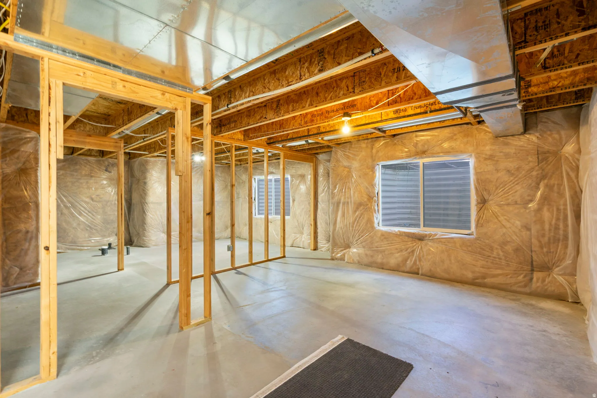 Unfinished basement featuring exposed wood framing, concrete flooring, and insulated walls