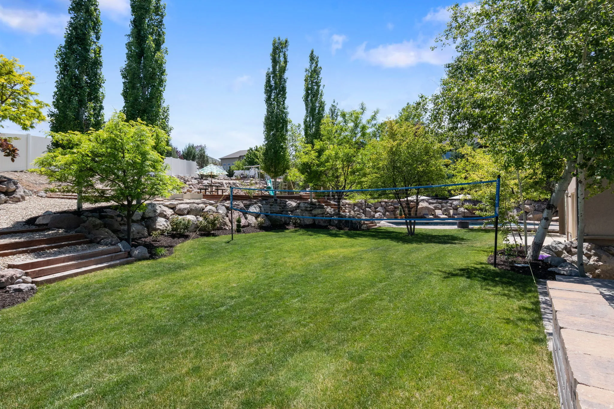 Expansive lawn area with a terraced landscape, mature trees, rock retaining walls, and tiered steps