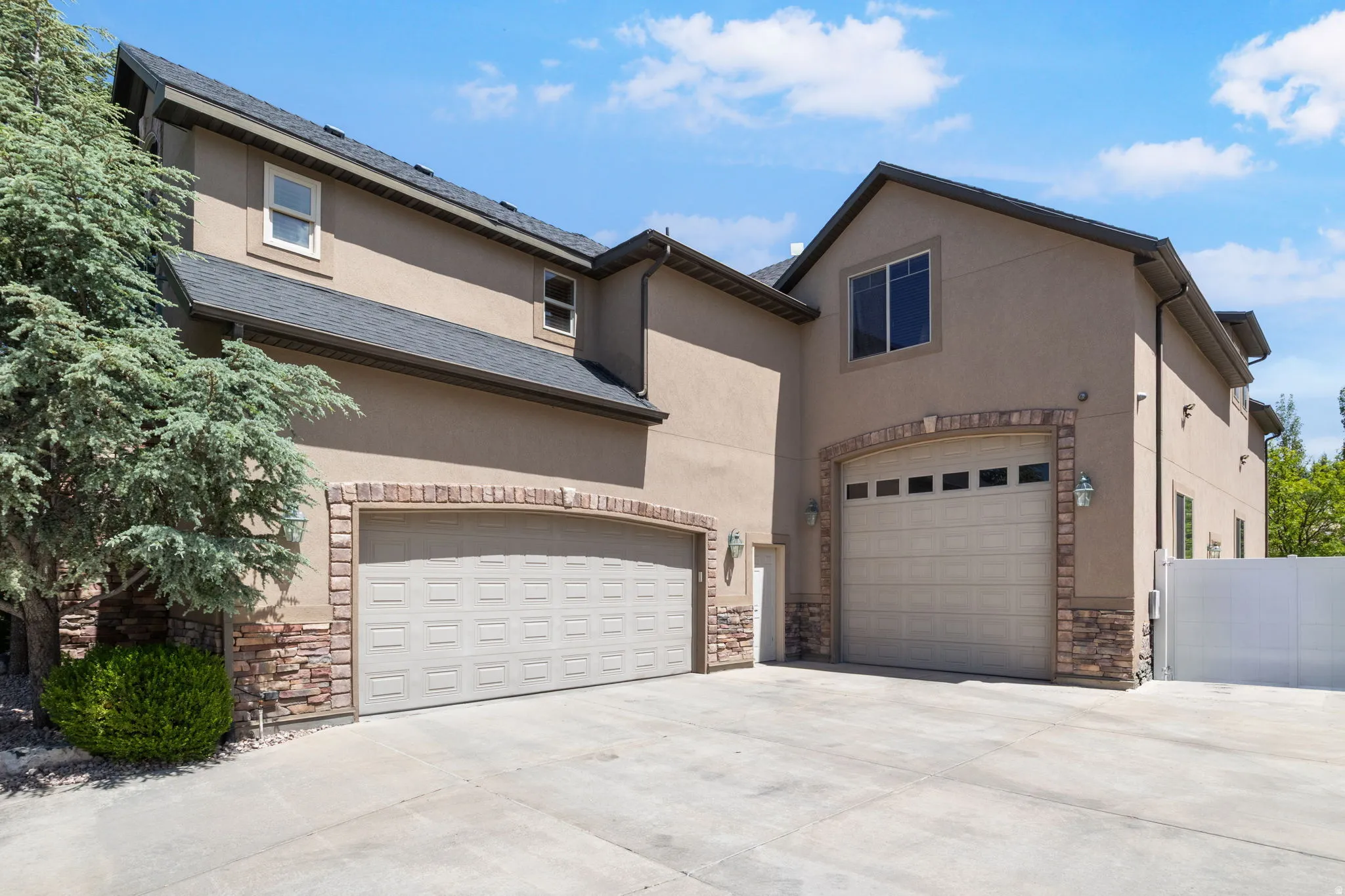 Exterior featuring stucco siding, stone accents, two attached garages, and an asphalt shingle roof