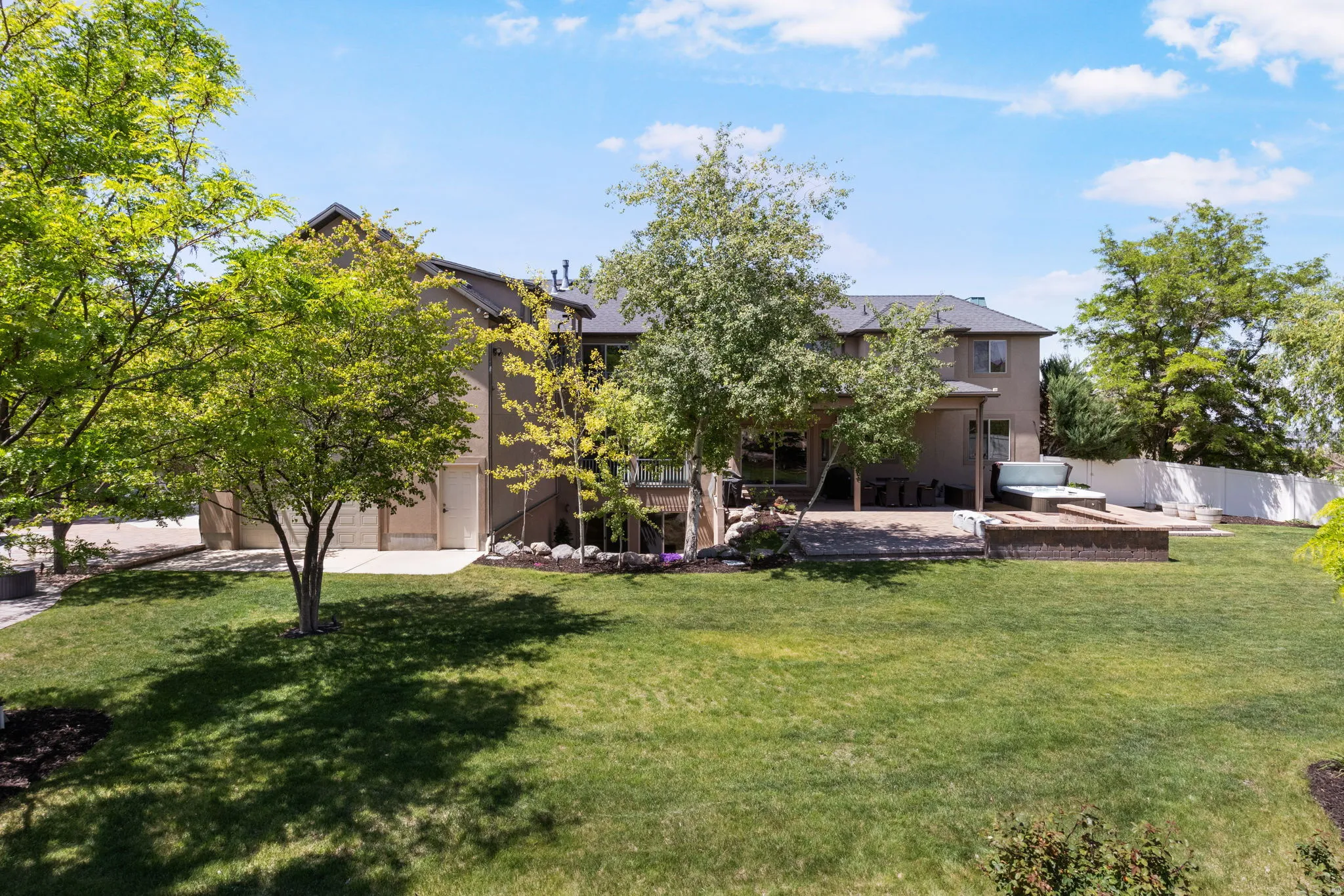 Expansive backyard featuring a manicured lawn, established trees, and a concrete patio