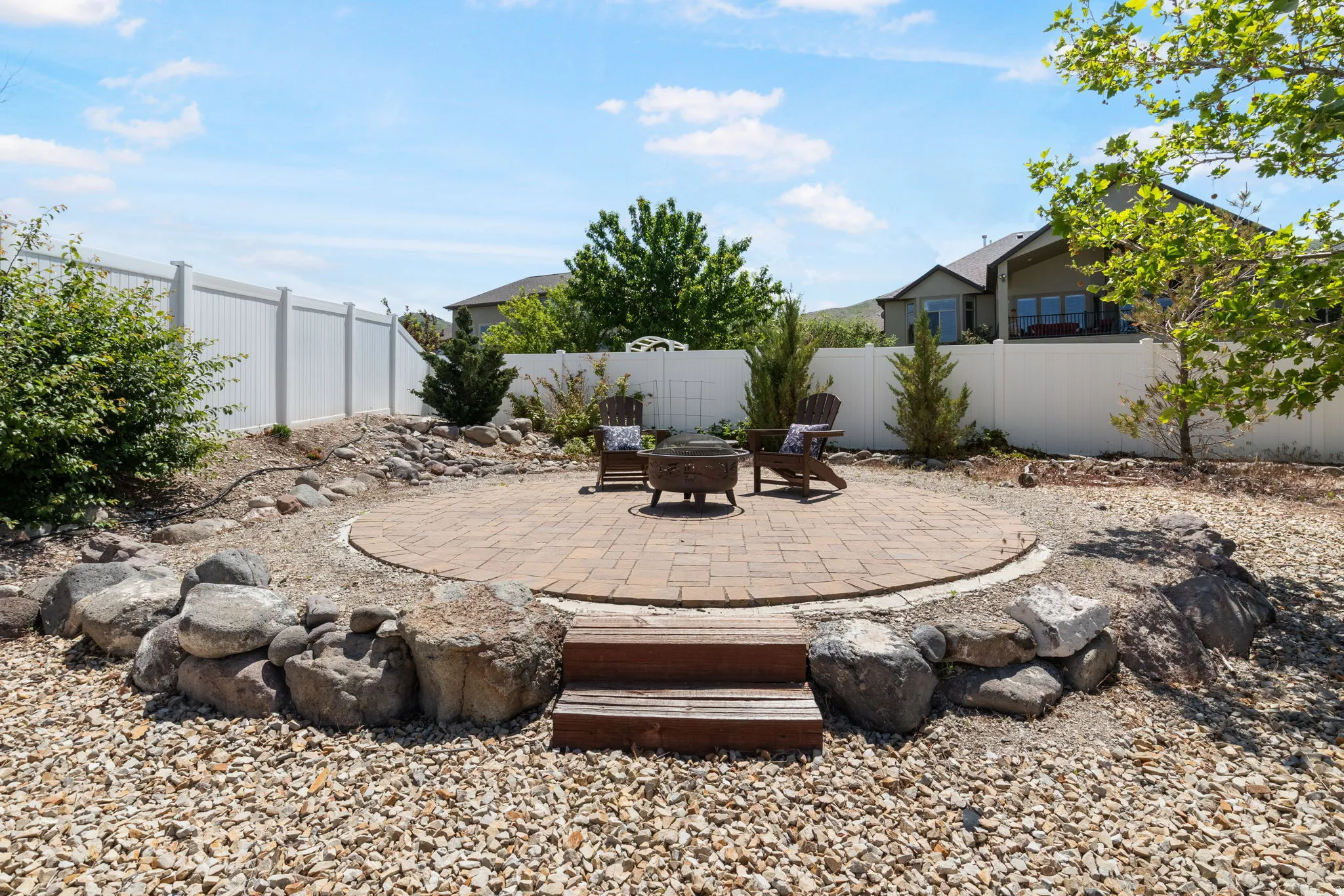 Up another terrace to the circular paver patio with a surrounding rock garden, privacy fencing, and mature landscaping.