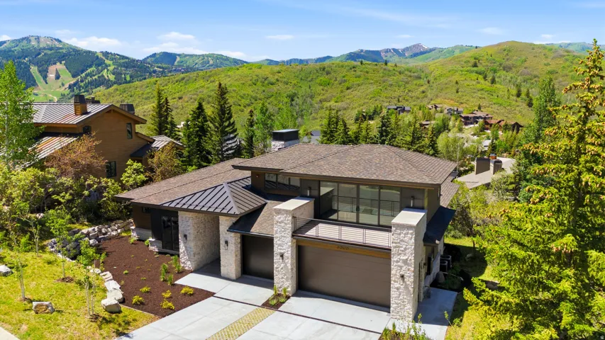 Modern architectural residence featuring stone facade accents, multiple garage bays, and an upper-level balcony