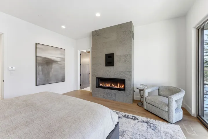Room featuring a linear fireplace with a stone-finish surround, wood-finish flooring, recessed lighting, and a full-height window