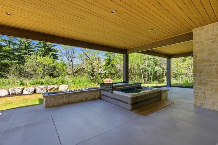 Covered patio featuring a built-in spa, stone retaining wall, and concrete flooring