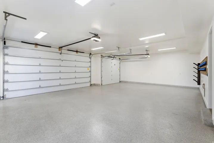 Spacious garage featuring two overhead doors, a speckled epoxy floor, bright overhead lighting, and white painted walls
