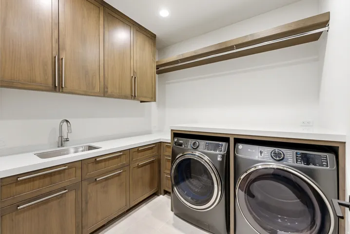 Dedicated laundry room featuring wood-finish cabinetry, white countertops, and an undermount sink with a gooseneck faucet