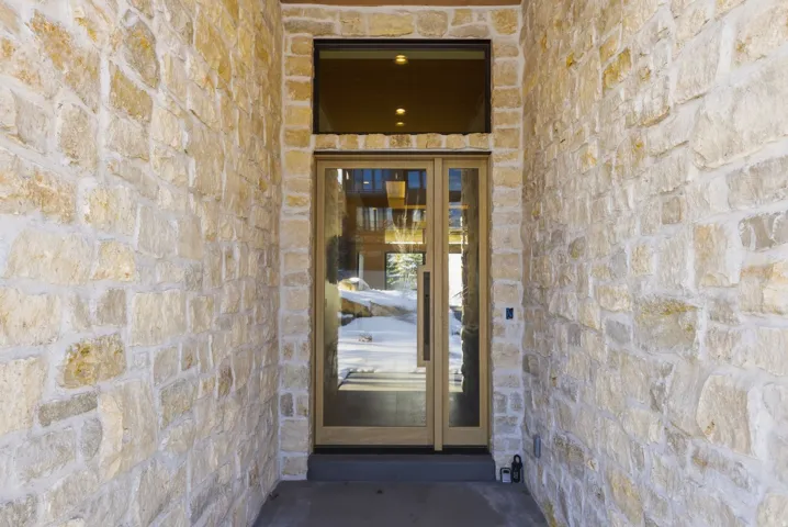 Stone veneer exterior facade with a wood-framed glass entry door and transom window