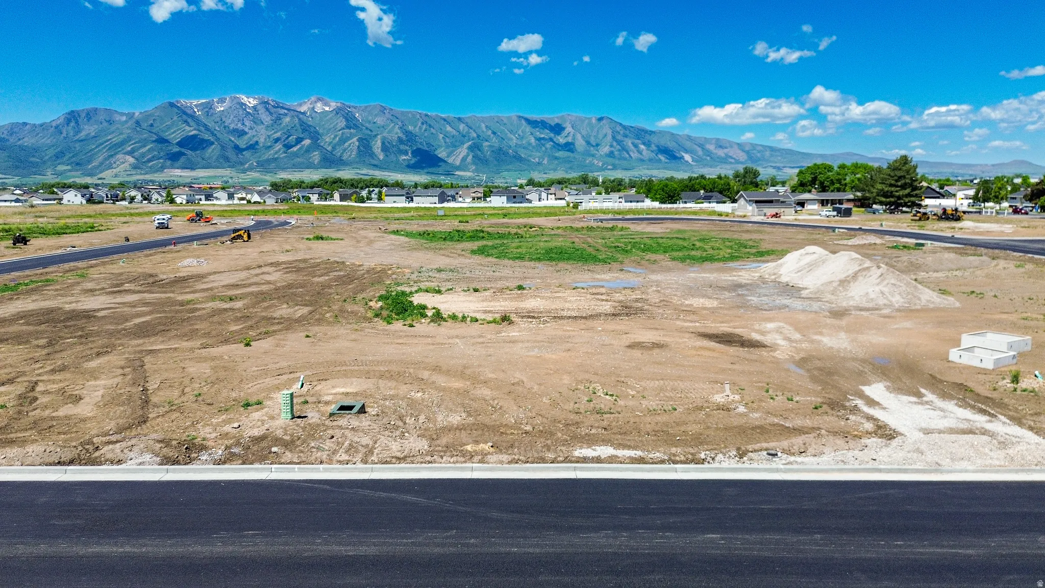 Expansive undeveloped land featuring a paved road frontage, visible utility connections, and distant mountain scenery