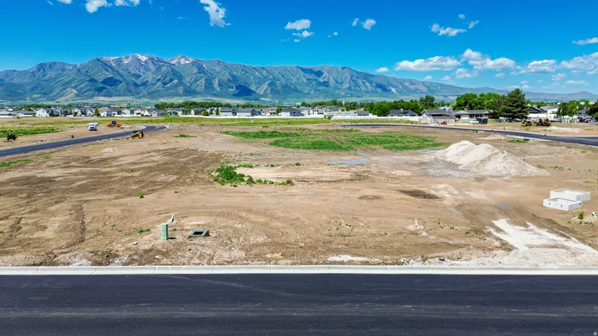 Expansive undeveloped land featuring a paved road frontage, visible utility connections, and distant mountain scenery