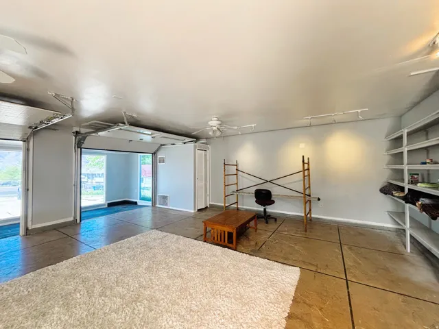 Spacious multi-purpose room featuring two overhead doors, built-in shelving, concrete flooring, and track lighting
