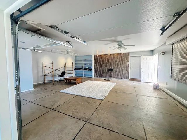 Spacious garage conversion featuring concrete slab flooring, a decorative wood-finish accent wall, and built-in shelving