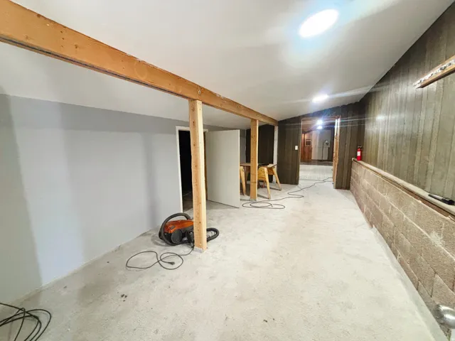 Spacious interior featuring exposed wooden beams, a partial concrete block wall, and concrete flooring