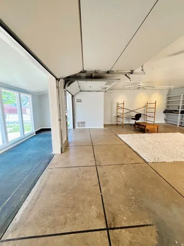 Spacious converted garage featuring scored concrete flooring, built-in shelving, a ceiling fan, and track lighting