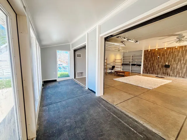 Interior space featuring concrete flooring, a sunroom with multiple windows, an accent wall with a wood-look finish, built-in shelving, and ceiling fans