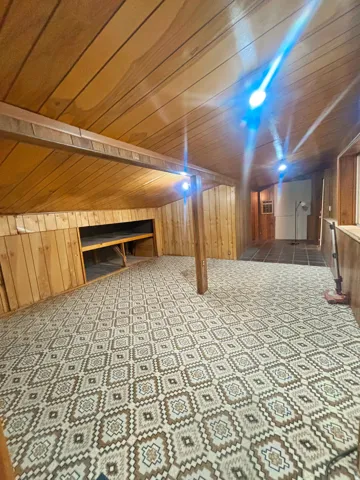 Room featuring wood-paneled walls and ceiling, patterned flooring, exposed support beam, and built-in shelving