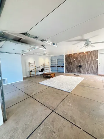 Spacious multi-purpose room featuring patterned concrete flooring, ceiling fans, built-in shelving, and a wood-finish accent wall