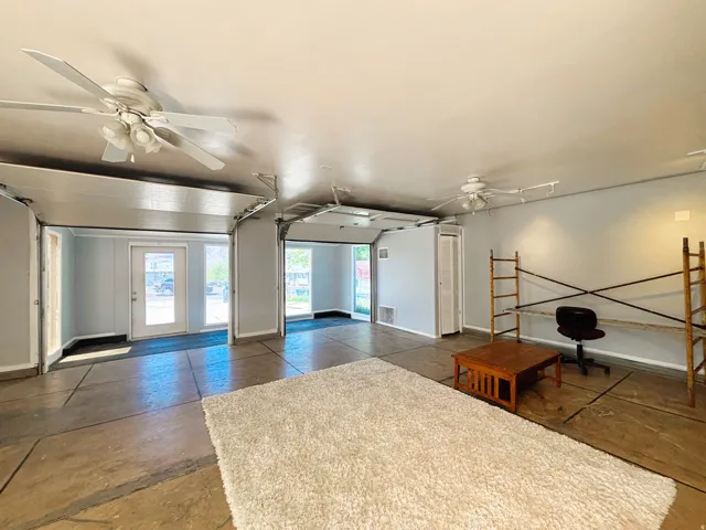 Spacious interior featuring two overhead garage doors, two ceiling fans, a white paneled door with glass inserts, and light gray wall paint