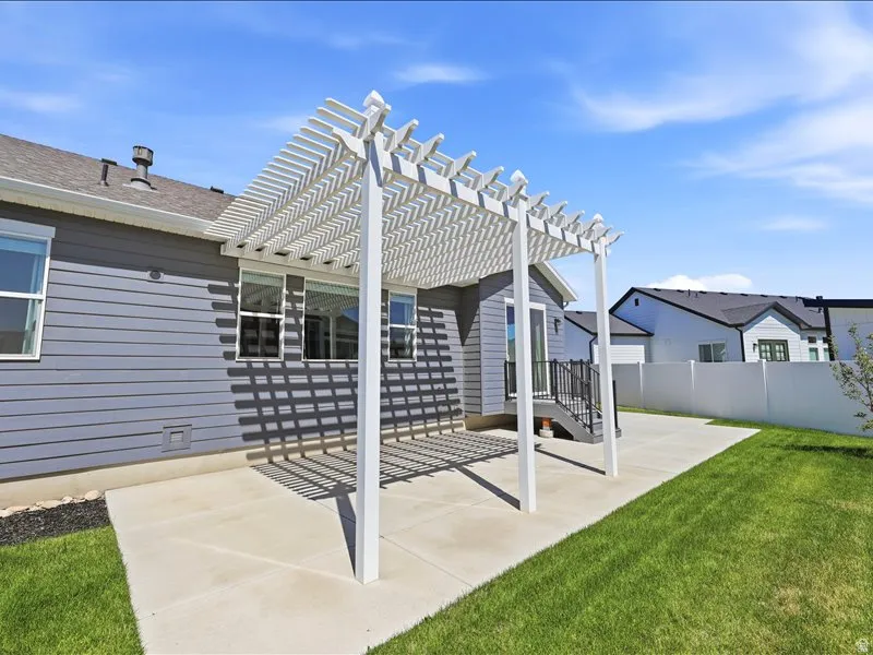 Expansive concrete patio featuring a white pergola structure and direct access to the interior via a glass sliding door