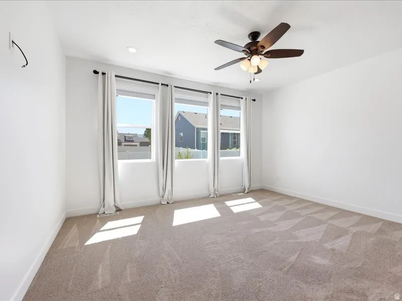 Bright room featuring three large windows, neutral carpet, a ceiling fan with integrated lighting, recessed lighting, and white walls