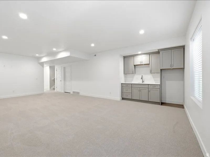Spacious carpeted room featuring a wet bar with gray cabinetry, white subway tile backsplash, and a stainless steel faucet