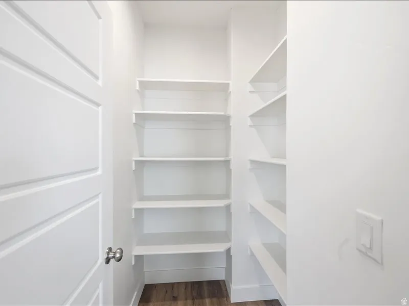 Walk-in pantry featuring extensive built-in shelving, wood-finish flooring, and a modern panel door with a brushed nickel knob