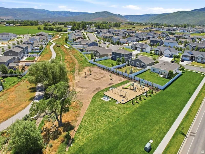 Expansive green space featuring a playground with swings and slides, a paved walking path, and mature trees