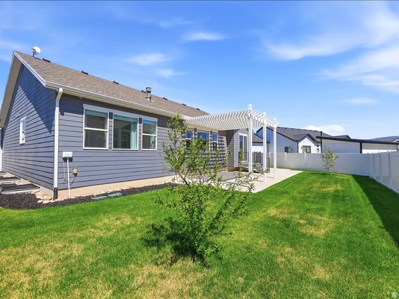 Expansive backyard featuring a manicured lawn, a white vinyl privacy fence, and a decorative pergola over a patio area