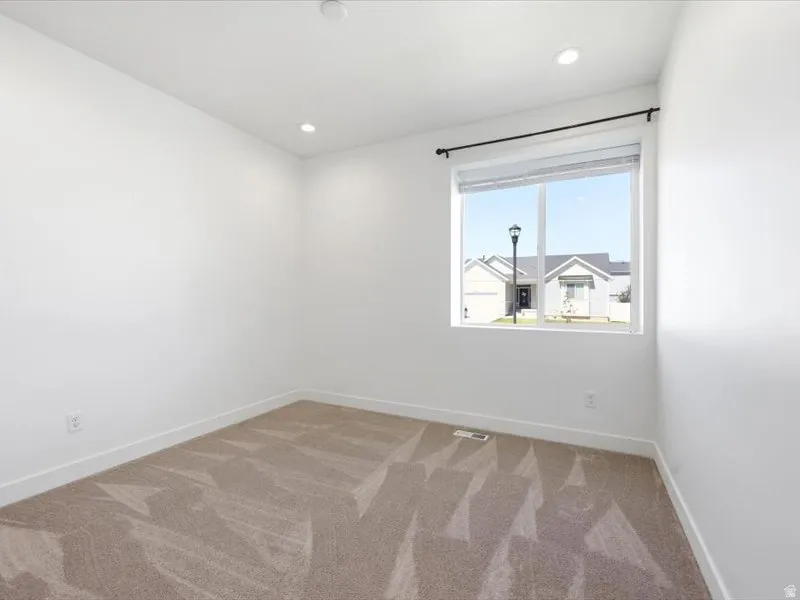 Bright interior space featuring a window with a black curtain rod, recessed ceiling lighting, and light-toned carpet flooring