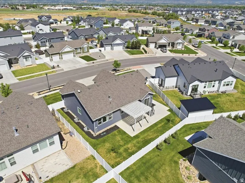 Rear exterior of a single-story residence featuring a gray pergola over a concrete patio, a manicured lawn, and white vinyl fencing