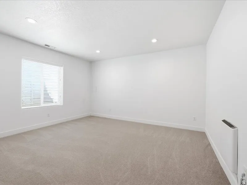 Spacious room featuring neutral carpeting, white walls, and a large window with horizontal blinds